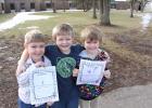 From left, Noah Dukes, Dakota Simoneau and Maverick McKenna show their Groundhog Day predictions with melting snow behind them at Staples-Motley Elementary School on Feb. 2. (Staples World photo by Mark Anderson)